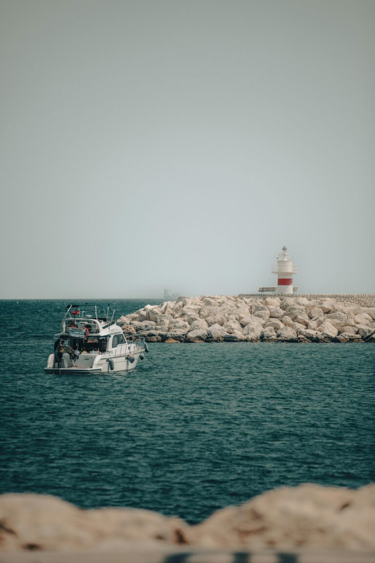 A serene ocean scene featuring a lighthouse, motorboat, and rocky shore.